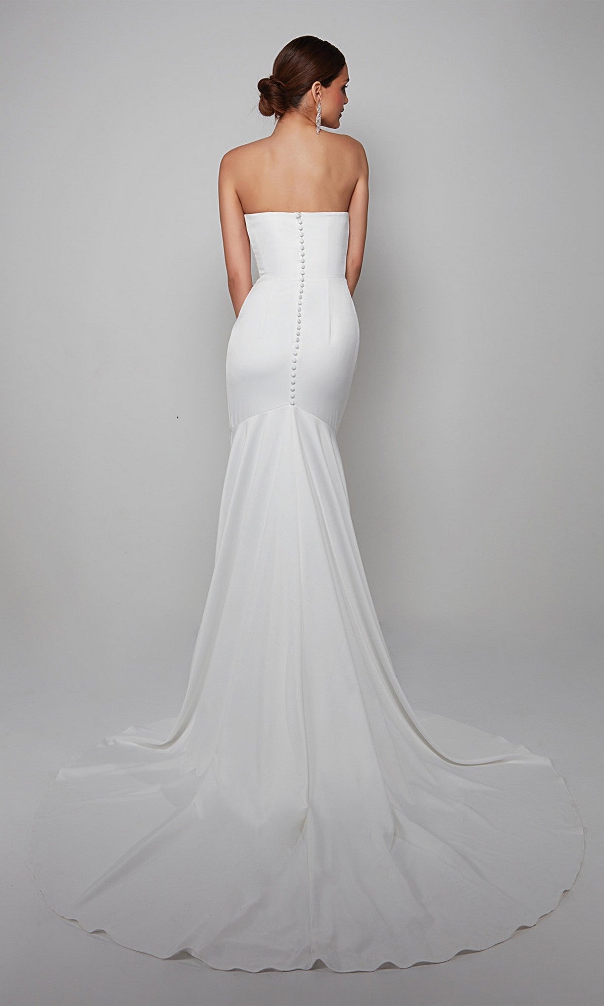 Woman wearing the Alyce 7057 long white dress, featuring a strapless design, button details down the back, and a flowing train, standing against a plain background.
